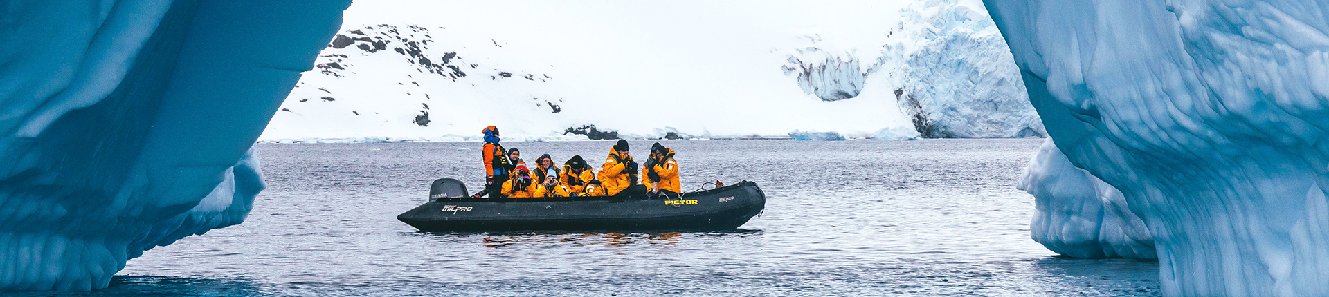 Group of people in a Zodiac boat framed by a large iceberg in Antarctica